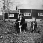 Svartvitt fotografi av Dan Andersson och en pojke som sitter på gräset utanför en Brunnsviks follhögskola.