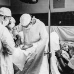 Svartvitt fotografi där tre operationspersonal står runt en patient täckt av vita lakan. En kirurg använder en kirurgsax i patientens öppna snitt. Bilden är från 1941.