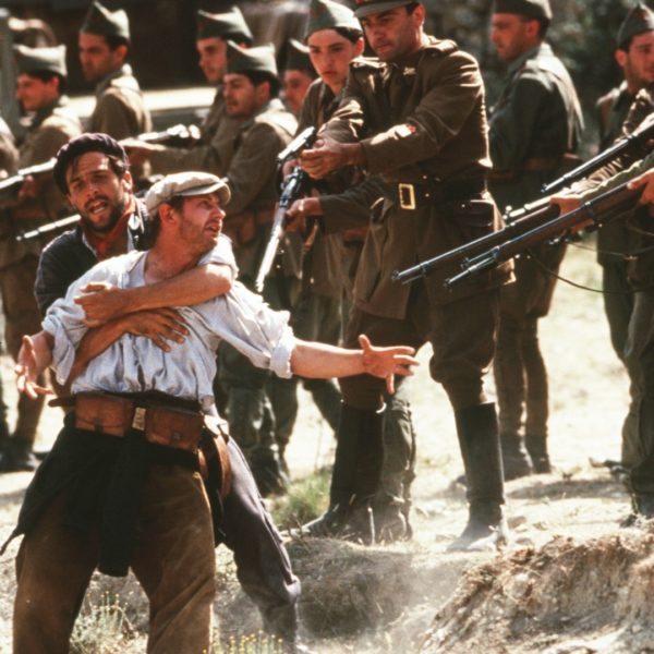 Stillbild från filmen Land och frihet. En man med sjal runt halsen håller om en man med vit skjorta. Soldater i uniformer pekar sina gevär mot dem.