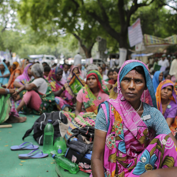 Kvinnliga bönder i färgglada saris sitter på marken i en av den senaste tidens många bondeprotester i Indien.