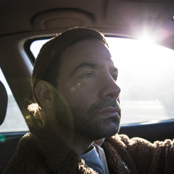 Pierro Dall’Osso fotograferad bakom ratten i sin bil, från passagerarsätet. Solen lyser in i sidorutan.