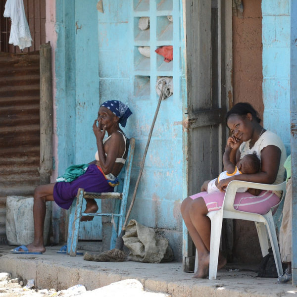 Två kvinnor sitter utanför ett bostadshus, den ena med ett litet barn i famnen.